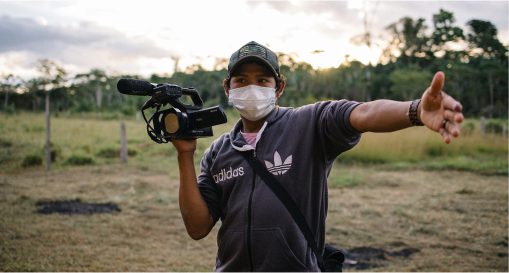 Tangai holding a camera, gesturing broadly