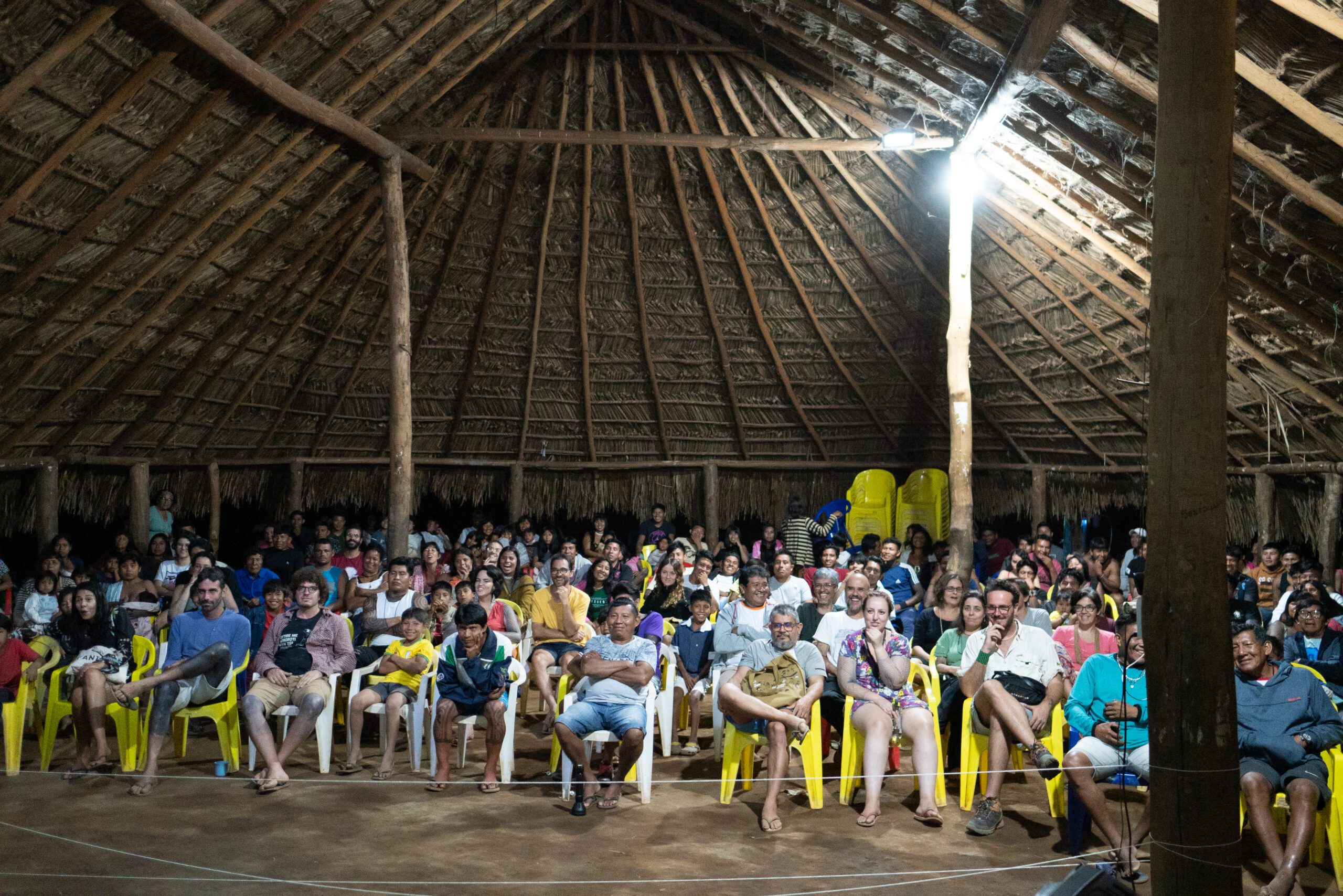 A group of people enjoying a screening of The Territory in a Maloca.